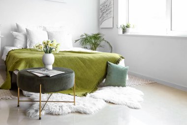 Işıl ışıl yatak odasının içinde rahat bir yatak odası ve pouf üzerinde narsis çiçekleri.