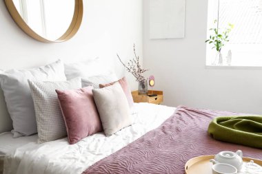 Yatak odasındaki sehpanın üzerinde bir sürü yastık ve çiçek açan ağaç dalları olan rahat bir yatak.