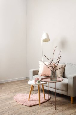 Oturma odasının içinde gri kanepe ve sehpanın üzerinde çiçek açan ağaç dalları var.