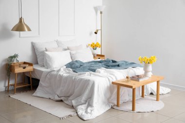 Yatak odasının içinde rahat bir yatak odası ve komodinin üzerinde narsis çiçekleri var.