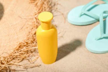 Güneş kremi, yaz şapkası ve kumdaki parmak arası terlikleri olan yaratıcı kompozisyon.