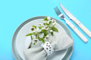 Katlanmış peçeteli ve turkuaz arka planda çiçek açan ağaç dallı güzel bir masa.