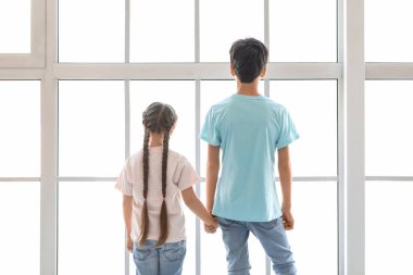 Küçük çocuk ve kız kardeşi pencerenin yanında el ele tutuşuyorlar.