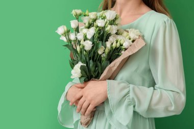 Yeşil arka planda güzel Eustoma çiçekleriyle dolu buketi olan genç bir kadın.