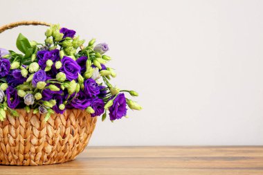 Beyaz duvarın yanındaki ahşap masada östoma çiçekli sepet.