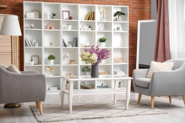 Oturma odasının içinde rahat koltuklar ve sehpanın üzerinde güzel leylak çiçekleri var.