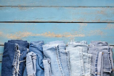 Mavi ahşap arka planda farklı bir kot pantolon, yakın plan.