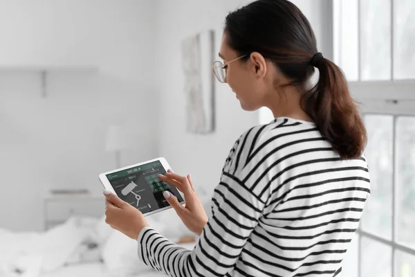 Young woman using smart home security system control panel in bedroom