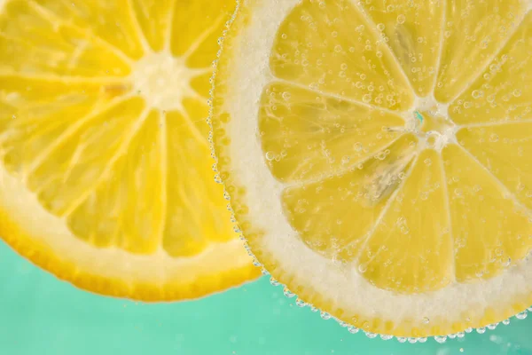 stock image Lemon slices in water with bubbles on turquoise background