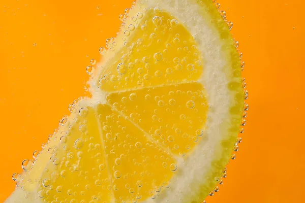 オレンジ色の背景に泡と水でレモンスライス — ストック写真