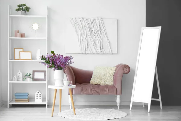 Interior of light living room with cozy armchair and lilac flowers on coffee table