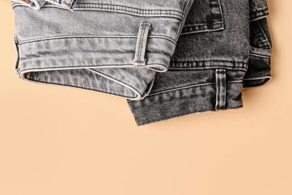 Different stylish folded jeans on pale orange background