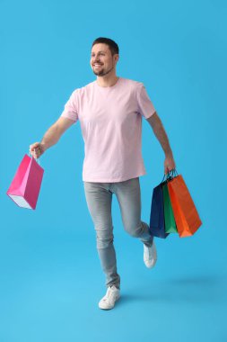 Mavi arka planda alışveriş torbaları olan yakışıklı bir adam.