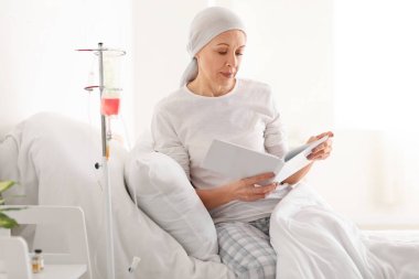 Kemoterapiden sonra klinikte kitap okuyan olgun bir kadın.