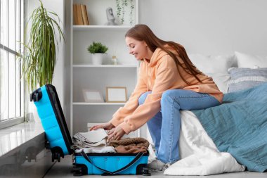 Genç bir kadın yatak odasında bavulunu boşaltıyor.