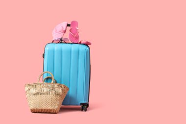 Pembe arka planda plaj aksesuarları olan bavul.
