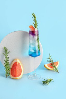 Bir bardak mor cin tonik ve mavi arka planda bir dilim greyfurt.
