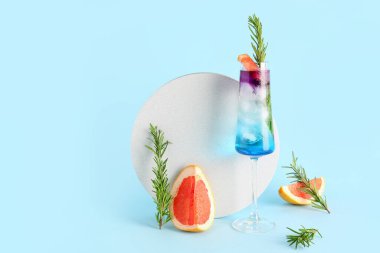 Bir bardak mor cin tonik ve mavi arka planda greyfurt.