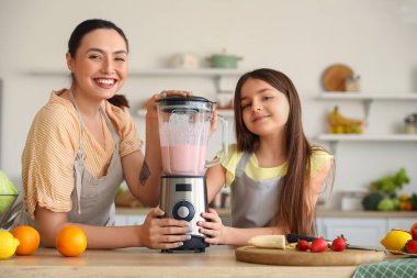 Küçük kız ve annesi mutfakta blender ile smoothie yapıyorlar.