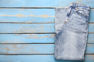 Stylish denim jeans on blue wooden background clipart