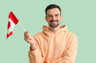 Yeşil arka planda Kanada bayrağı taşıyan yakışıklı bir adam.