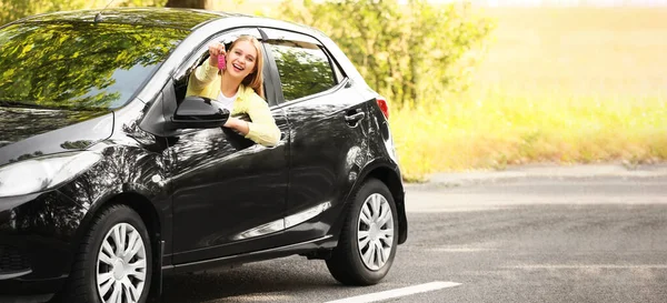Happy young woman with key sitting in new car