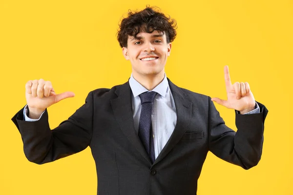 黄色の背景に負け犬のジェスチャーを示す若いビジネスマン — ストック写真