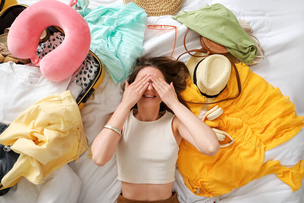 Молодая женщина с пляжными принадлежностями и чемоданом лежит на кровати