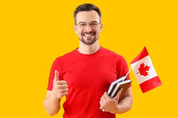 Przystojny Mężczyzna Flagą Kanady Książkami Przedstawiającymi Kciuk Góry Żółtym Tle — Zdjęcie stockowe
