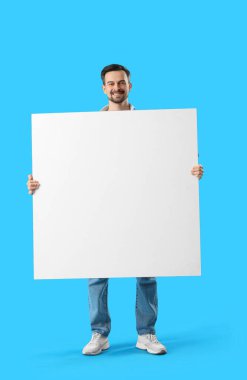 Mavi arka planda kocaman boş posteri olan yakışıklı bir adam.