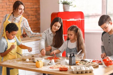 Mutfakta aşçılık kursu sırasında pizza hazırlayan bir grup küçük çocukla birlikte kadın şef.