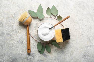 Bir kase kabartma tozu, temizlik fırçası, sünger ve grunge arkaplanda okaliptüs dallarıyla kompozisyon