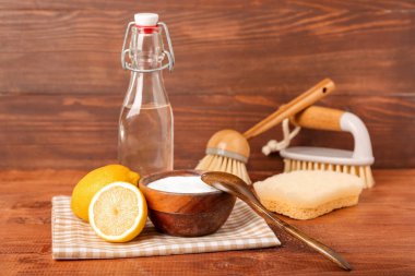 Tahta arka planda bir kase kabartma tozu, limon, sirke ve temizlik malzemesi.