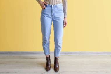 Young woman in stylish jeans near yellow wall clipart