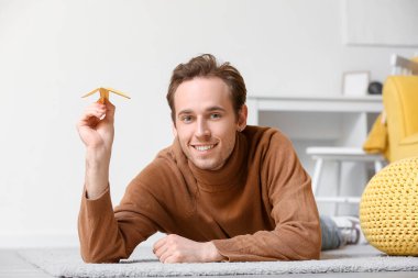 Evinde yerde yatmakta olan kağıt uçakla genç bir adam.