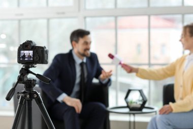 Mikrofonlu kadın gazeteci ofiste kamera önünde adamla röportaj yapıyor, yakın plan.