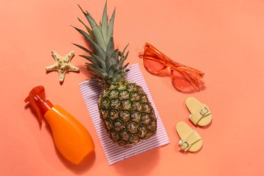 Kırmızı arka planda güneş kremi, denizyıldızı, parmak arası terlik ve güneş gözlüğü olan ananas.