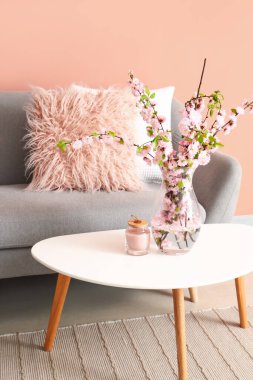 Oturma odasının içindeki sehpanın üzerinde çiçek açan sakura dalları olan vazo.