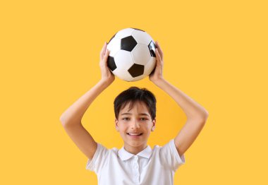 Sarı arka planda futbol topu olan küçük çocuk.