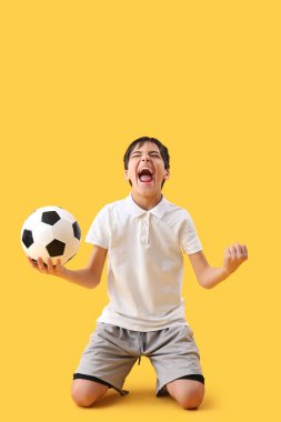 Sarı arka planda futbol topu olan mutlu küçük çocuk.