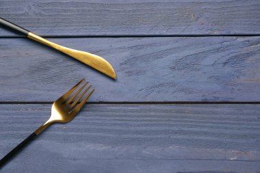 Mavi ahşap arka planda siyah saplı altın çatal ve bıçak.