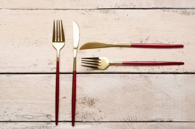 Beyaz ahşap arka planda kırmızı saplı altın çatallar ve bıçaklar.