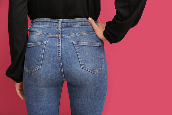 Молодая женщина в стильных джинсах на красном фоне, вид сзади