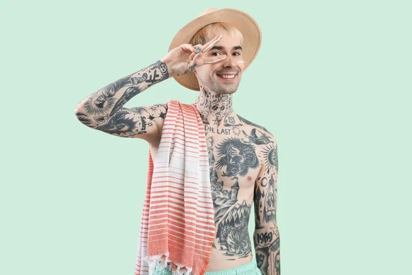 Tattooed man applying sunscreen cream on light green background