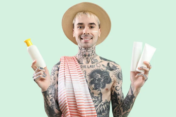 Tattooed man with sunscreen creams on light green background
