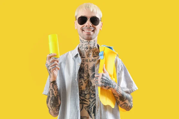 Tattooed man with paddles and sunscreen cream on yellow background