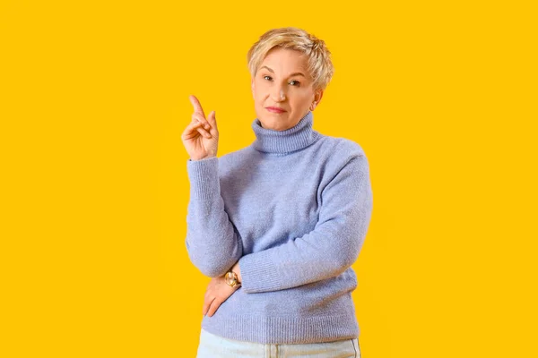 Nachdenkliche Reife Frau Zeigt Auf Etwas Auf Gelbem Hintergrund — Stockfoto