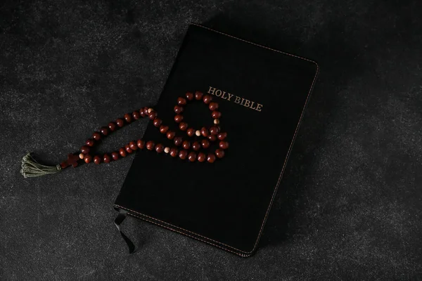 Holy Bible with prayer beads on black background