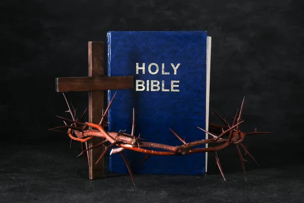 Holy Bible with crown of thorns and cross on black background