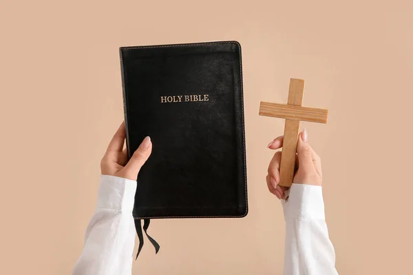 聖書を持つ女性の手と薄いオレンジの背景にクロス — ストック写真